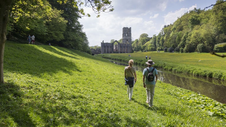 Two visitors walk through the grounds of Fountains Abbey, North Yorkshire